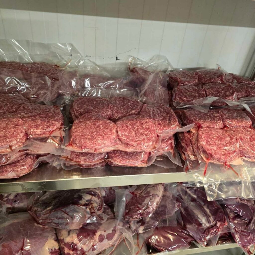 Vacuum-sealed packages of raw red meat arranged on metal refrigerator shelves.