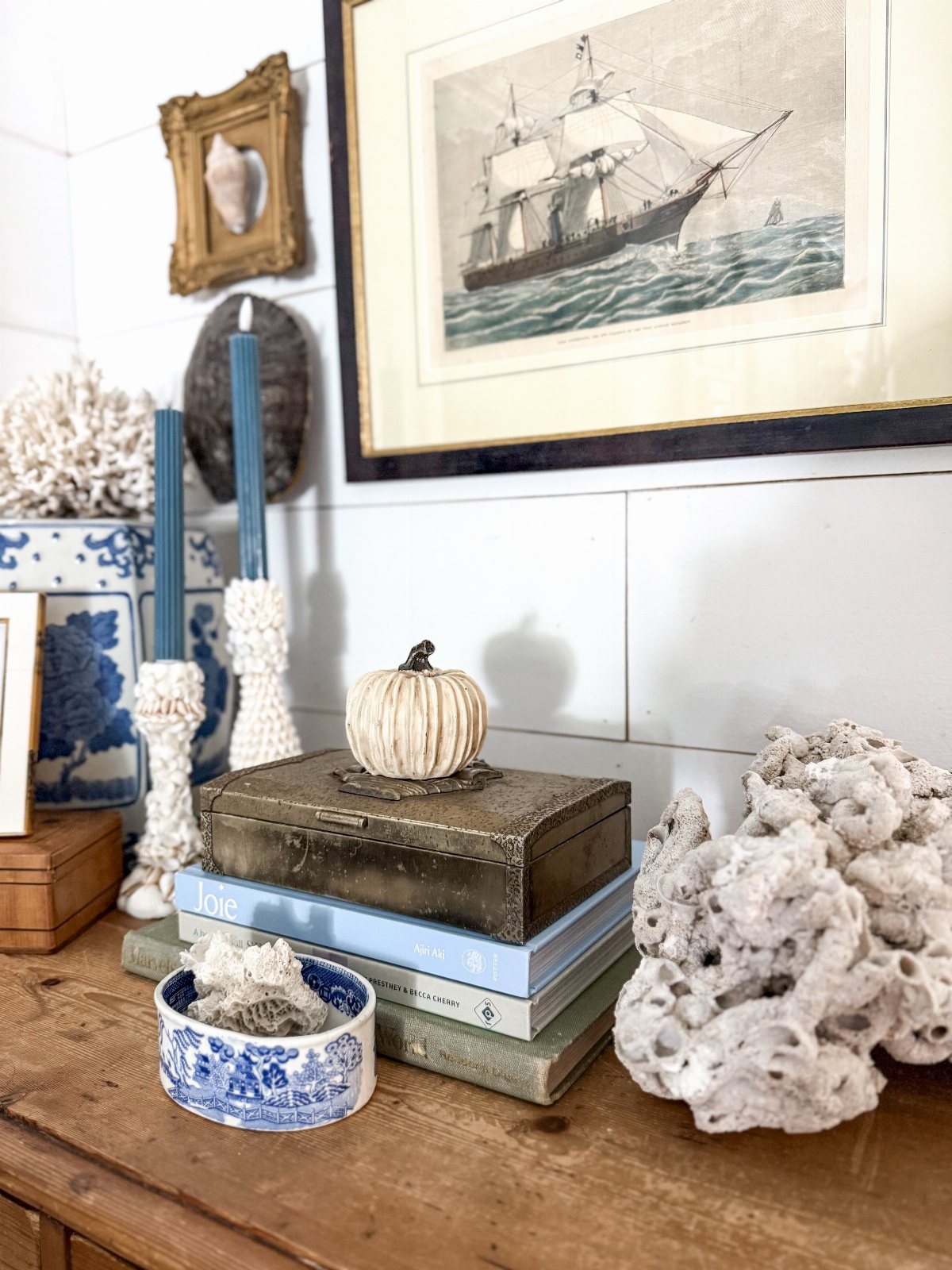Coastal decor items including white coral, blue patterned ceramics, and a vintage ship print on a wooden surface.