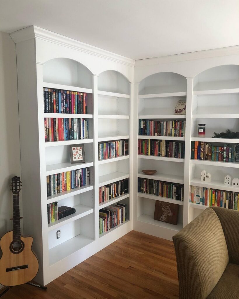 Large white built-in corner bookcases filled with many colorful books in a room.