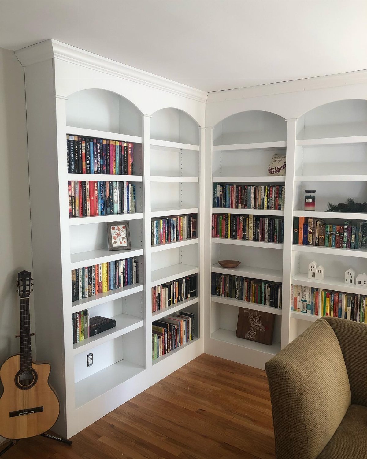 Large white built-in corner bookcases filled with many colorful books in a room.
