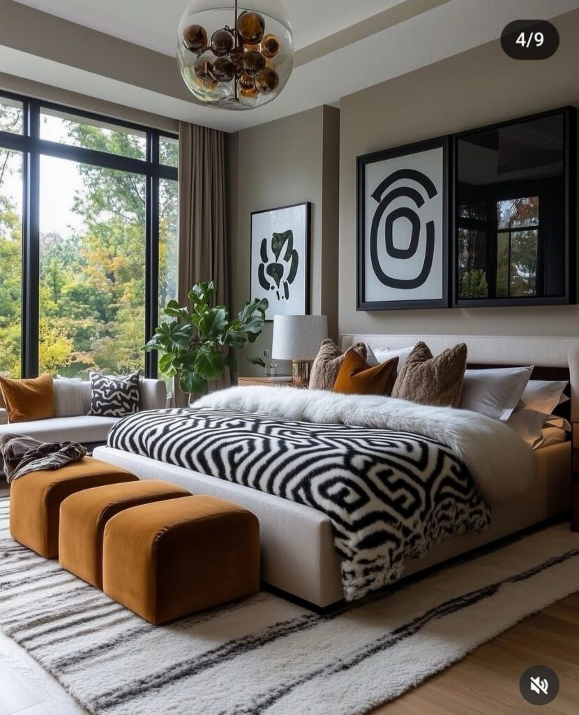 Modern bedroom with black and white patterned bedding, cream headboard, and brown velvet ottomans.