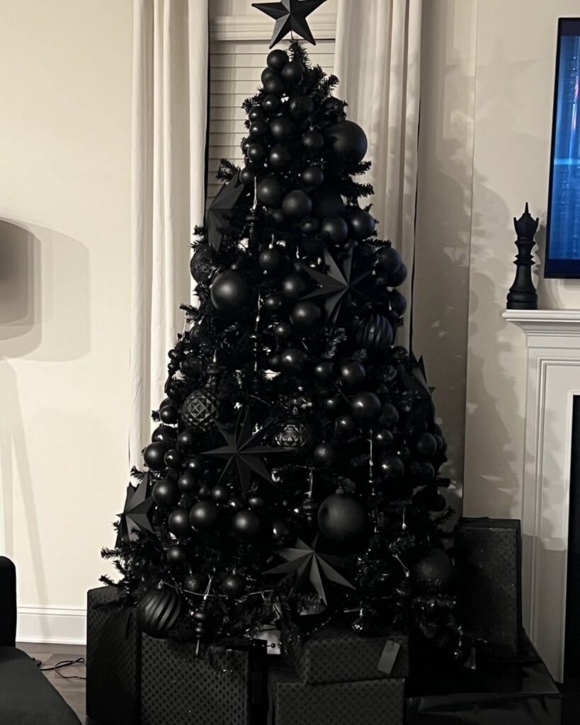 A black Christmas tree decorated with various black ornaments and stars sitting near a white fireplace.