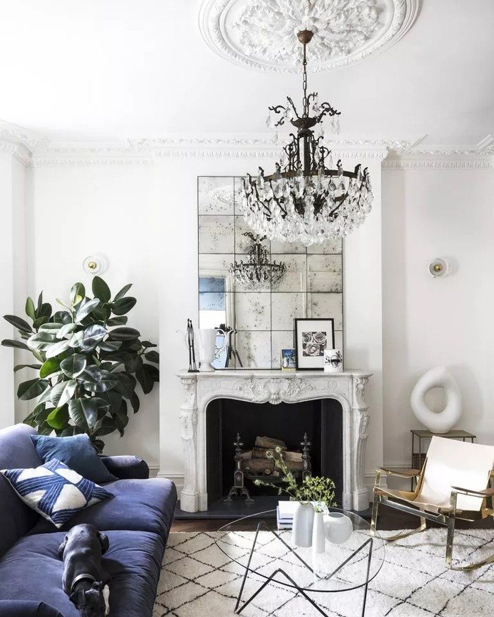 Navy blue sofa and white fireplace in a bright living room with a crystal chandelier.