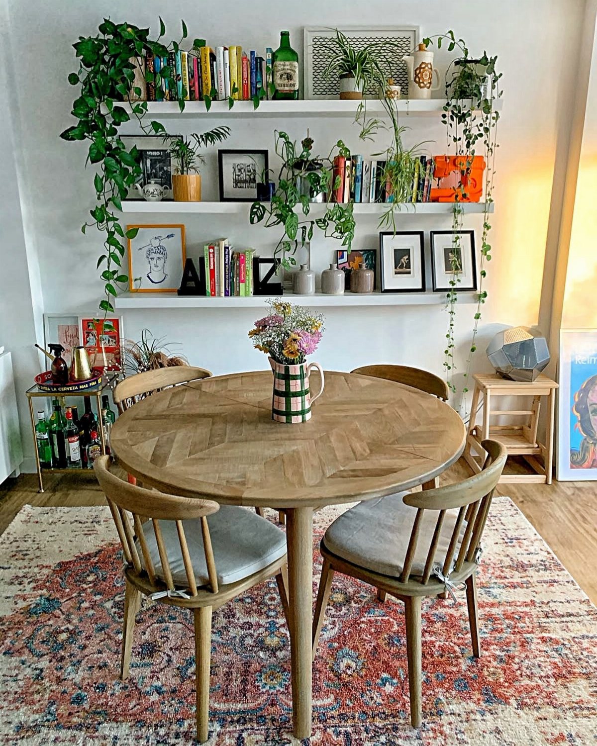 Wooden dining table and chairs set against shelves filled with books and plants.