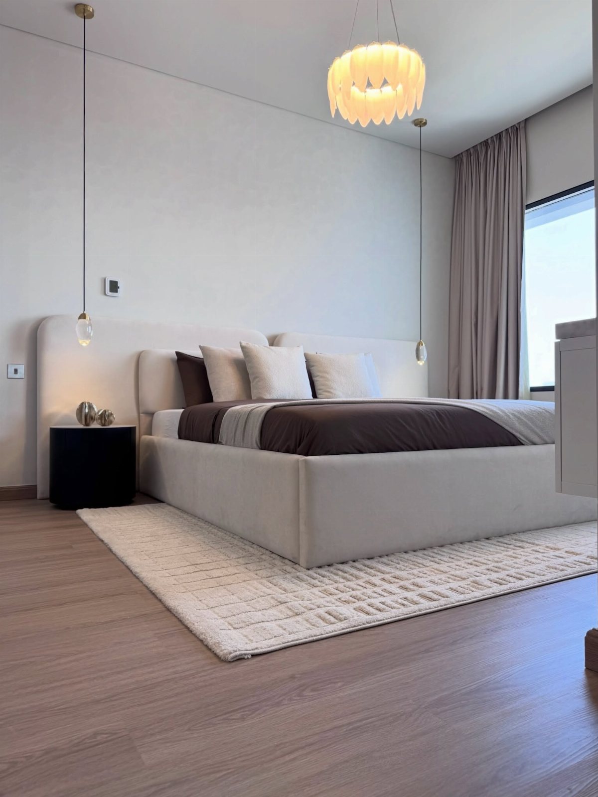 Modern bedroom with a white upholstered bed, brown bedding, and neutral decor on wood floors.