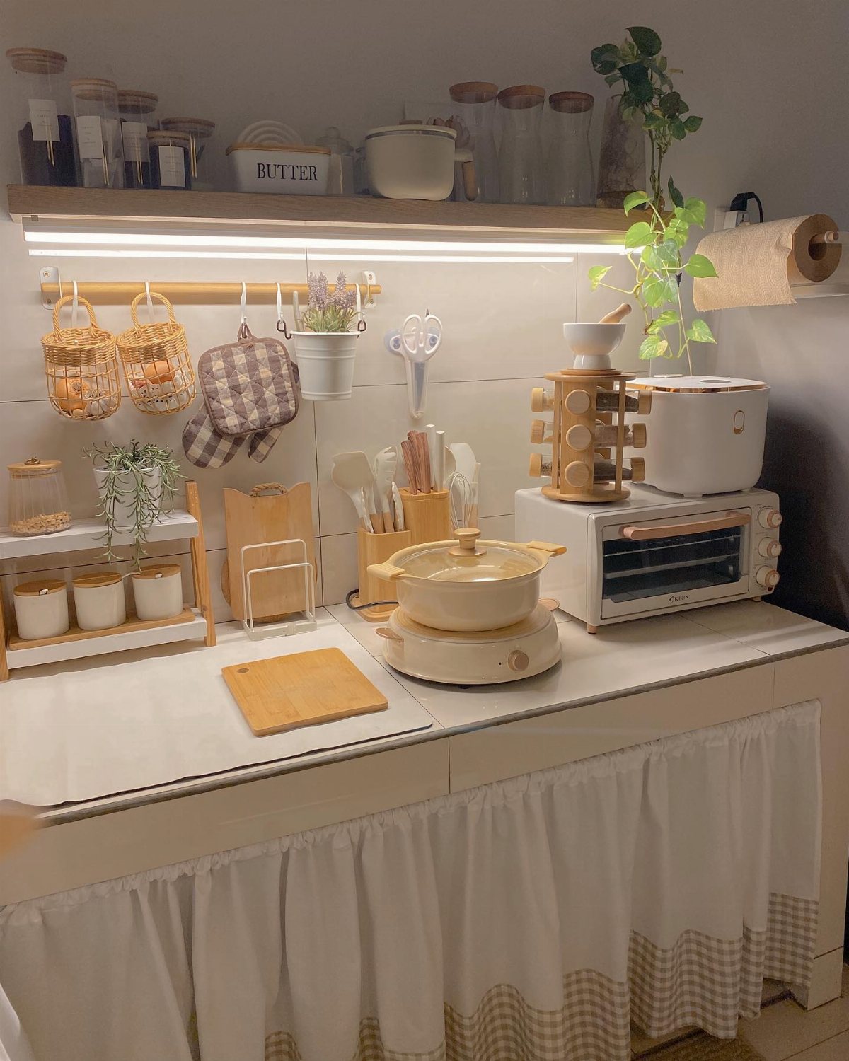 Organized kitchen counter with cream appliances, wooden accents, small plants, and warm under-shelf lighting.