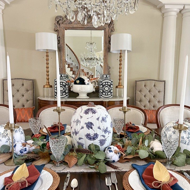 A fall dining table set with a large blue floral pumpkin centerpiece and elegant tableware.