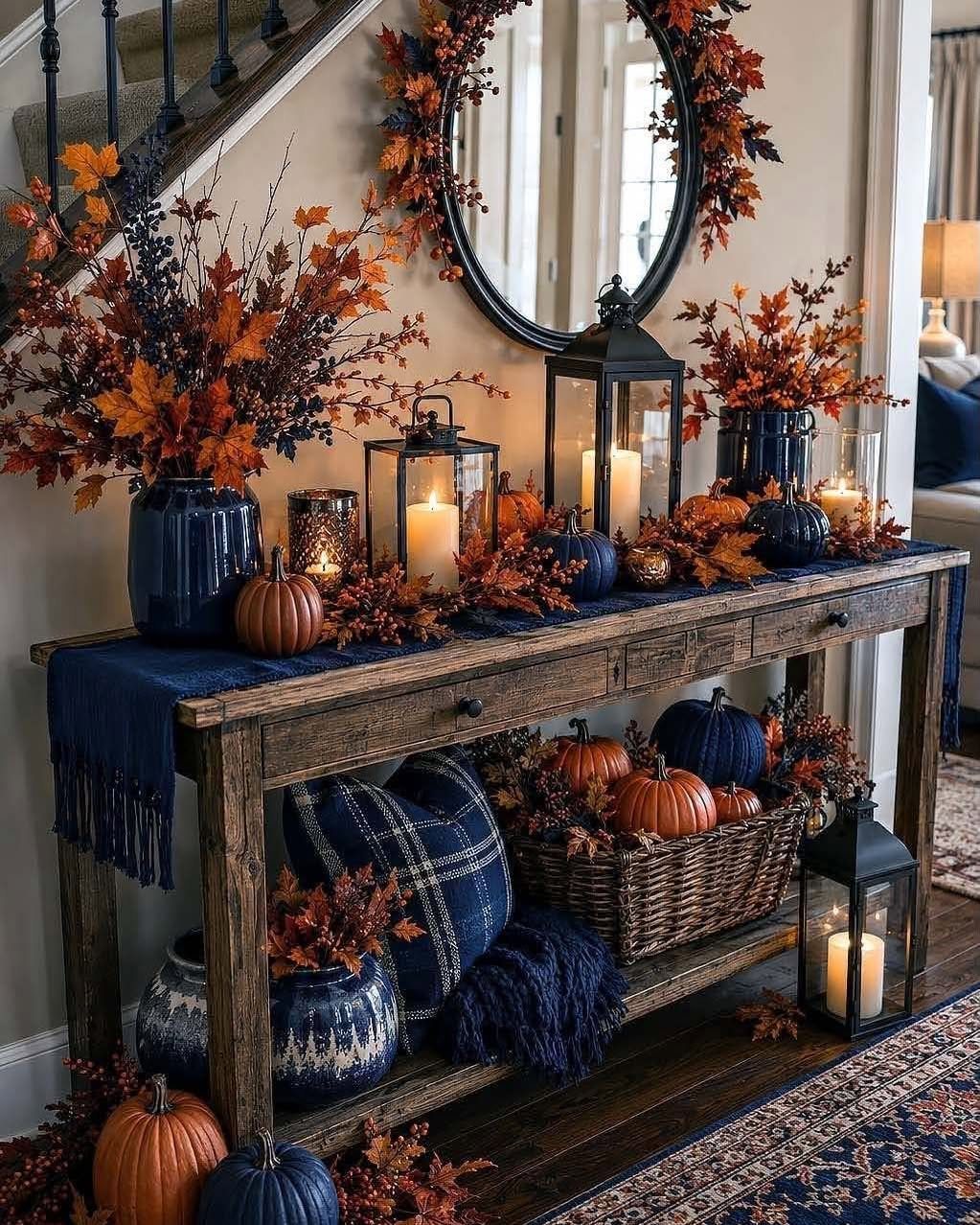 A wooden entry table decorated with navy blue accents, orange autumn leaves, pumpkins, and glowing lanterns.