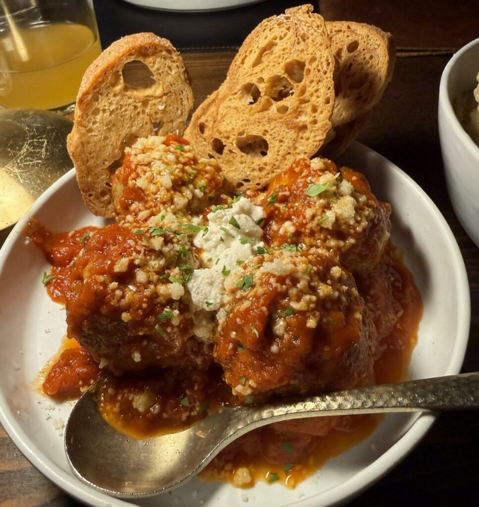 Meatballs in red tomato sauce with parmesan cheese and toasted baguette slices in a white bowl.