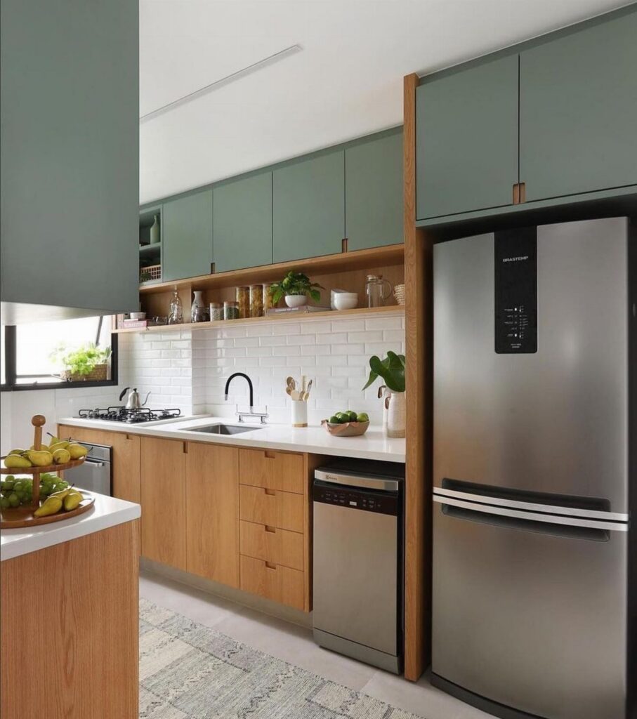Modern kitchen with sage green upper cabinets, wooden lower cabinets, and a stainless steel refrigerator.