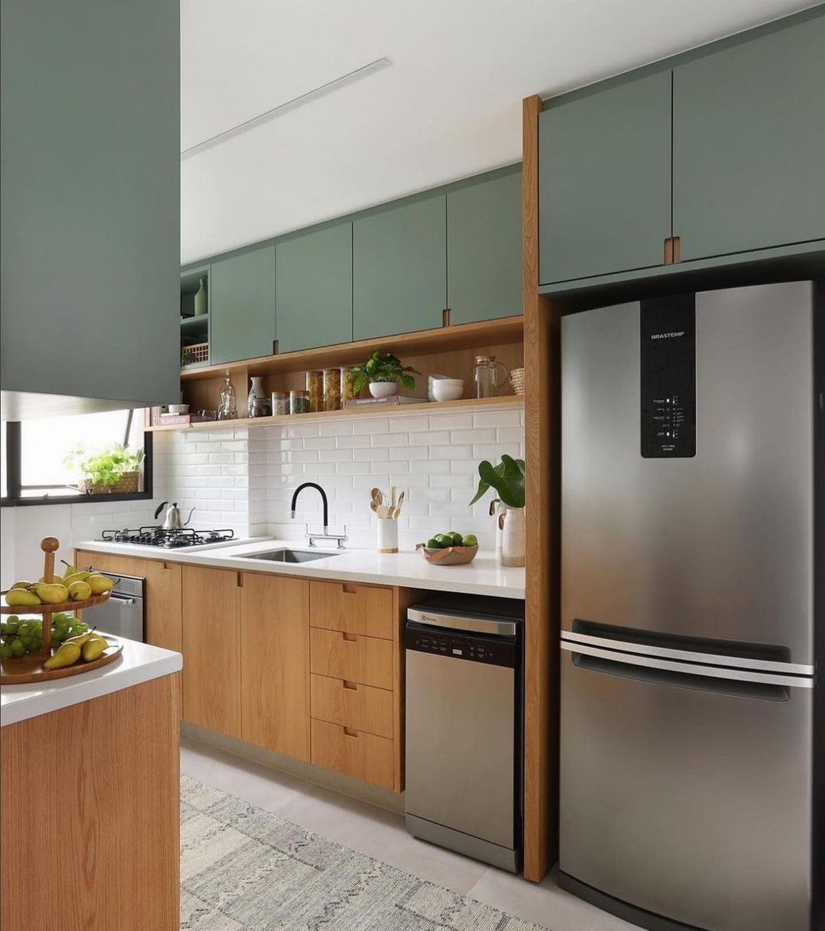 Modern kitchen with sage green upper cabinets, wooden lower cabinets, and a stainless steel refrigerator.