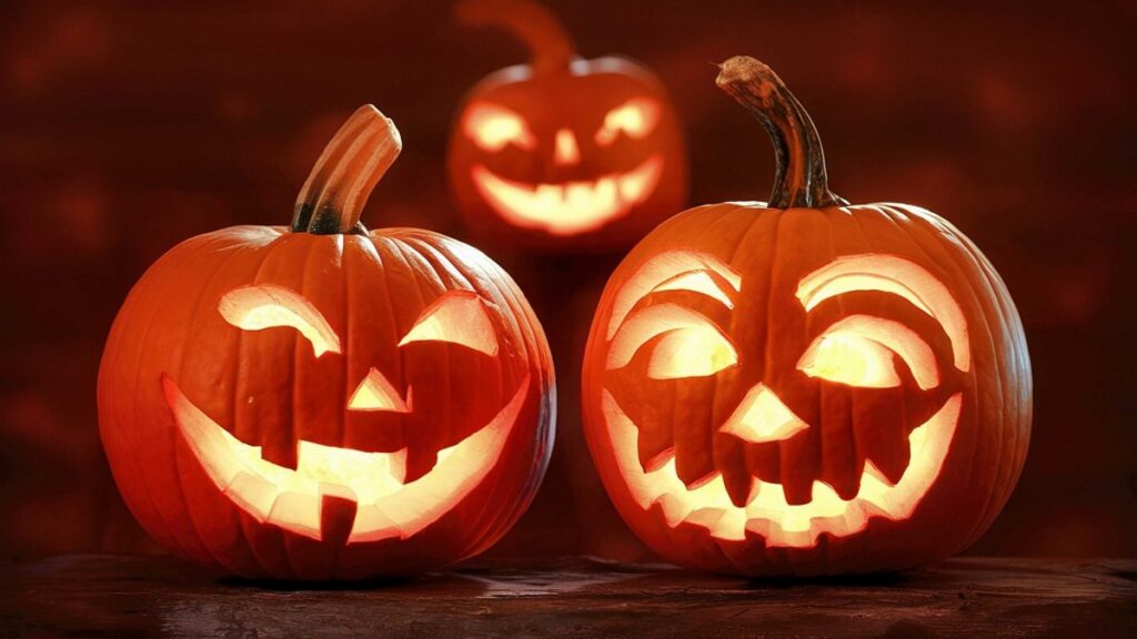 Three glowing carved jack-o'-lanterns with various facial expressions sitting on a dark wooden surface.