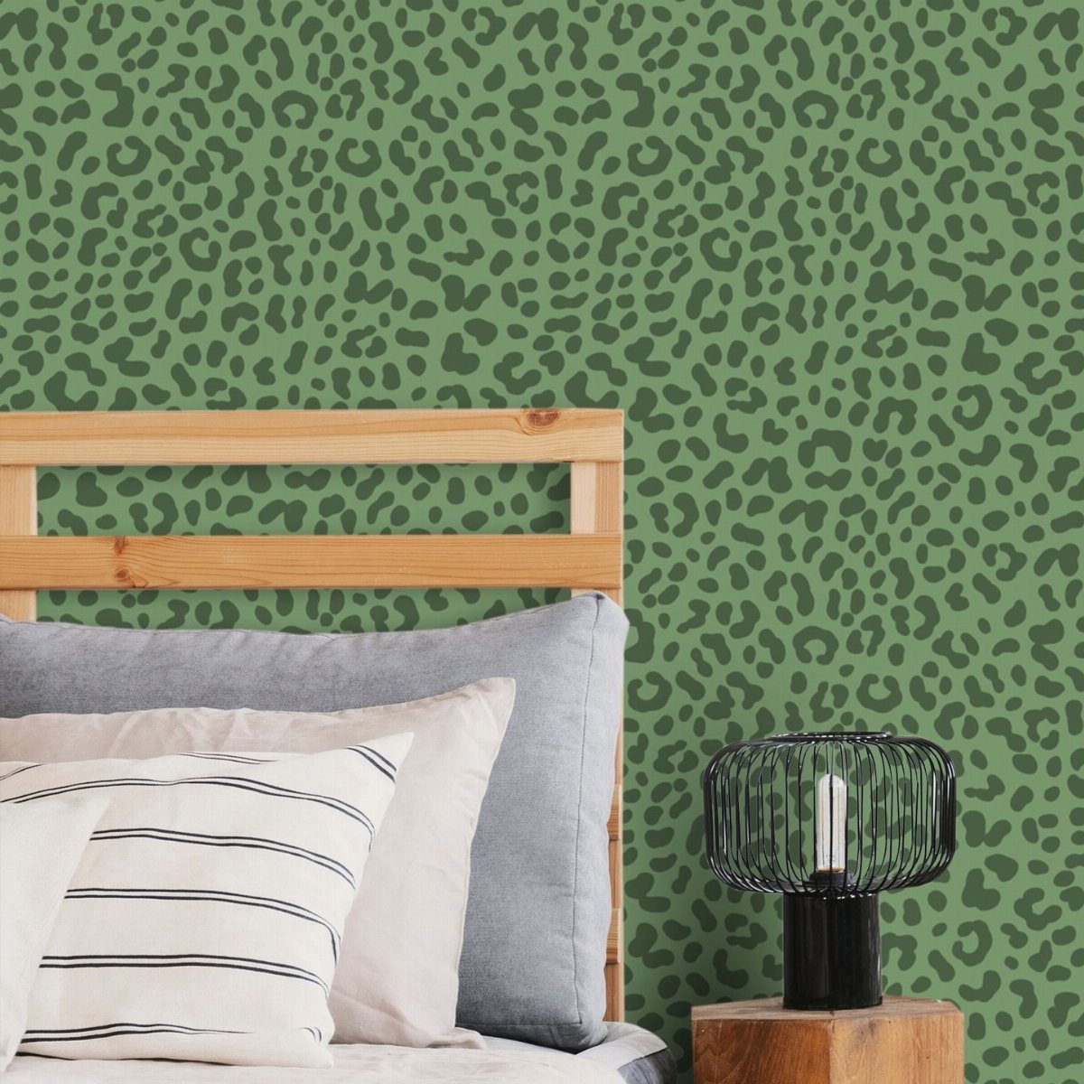 Green leopard print wallpaper behind a wooden bed frame with striped pillows and a black lamp.
