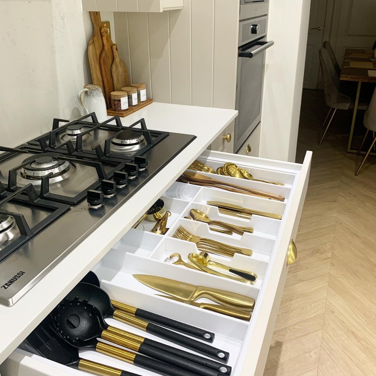Gold and black kitchen utensils organized in a white drawer compartment system.