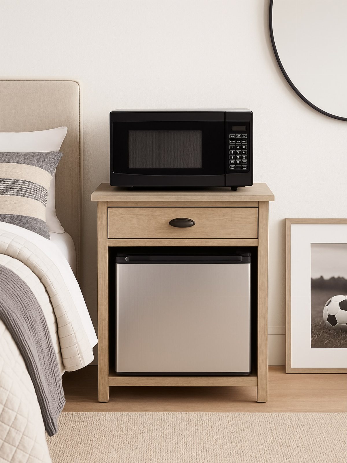 A light wood nightstand holding a black microwave with a silver mini fridge underneath.