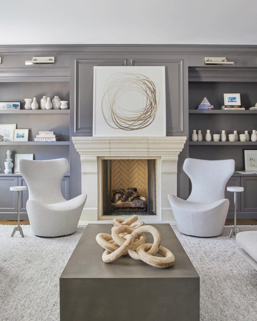 Modern grey living room with built-in shelves, a white fireplace, and two grey armchairs.