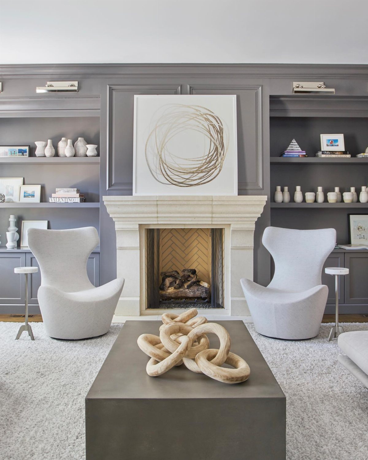 Modern grey living room with built-in shelves, a white fireplace, and two grey armchairs.