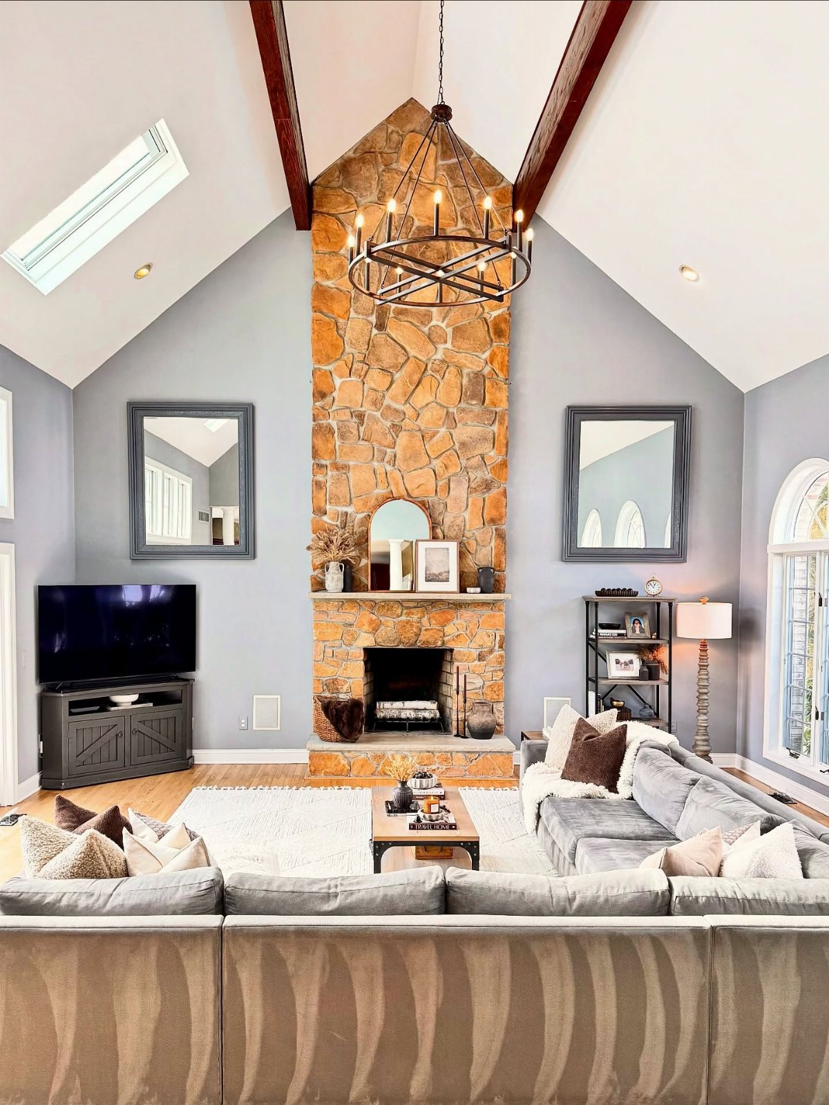 A neutral living room featuring a tall stone fireplace, grey walls, and a large sectional sofa.