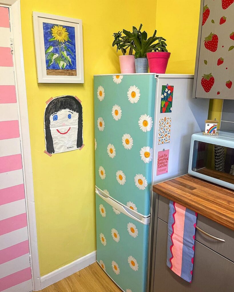Light blue refrigerator decorated with white daisy patterns against a bright yellow wall.