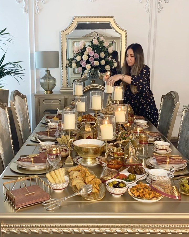 A decorated dining table with gold plates, various food dishes, and large white candles.