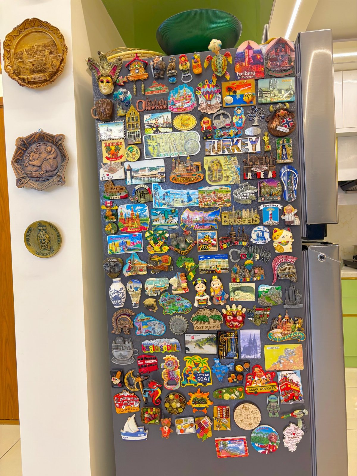 A stainless steel refrigerator densely covered in many colorful souvenir magnets of various shapes and sizes.