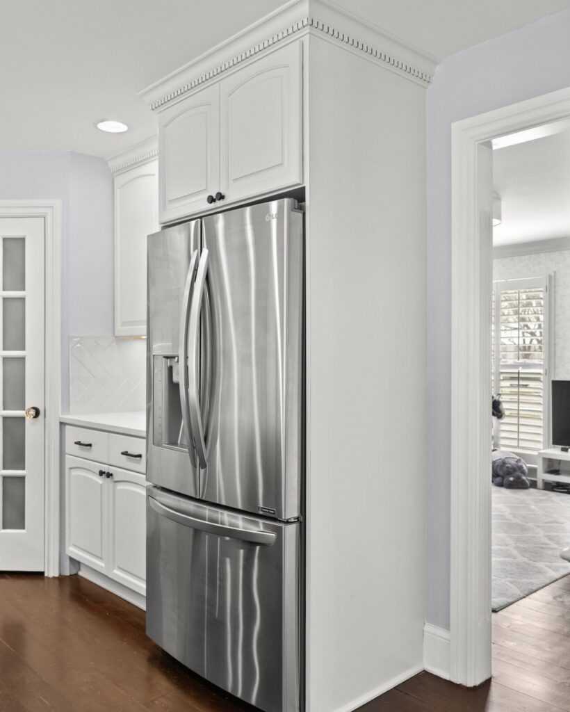 Stainless steel refrigerator built into white kitchen cabinetry with a seamless side panel design.