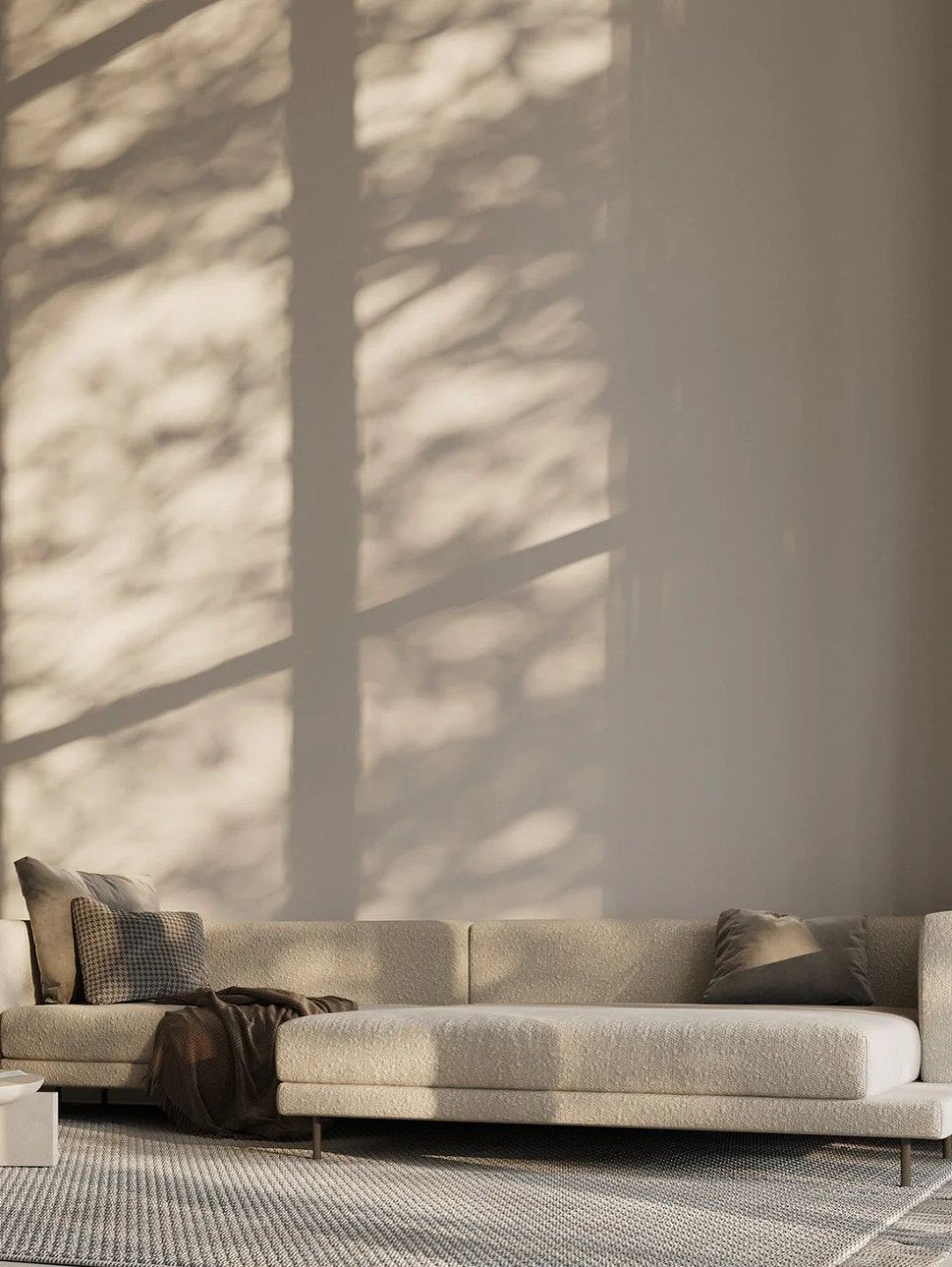 Cream textured sofa with neutral pillows and a brown throw under tree shadows.