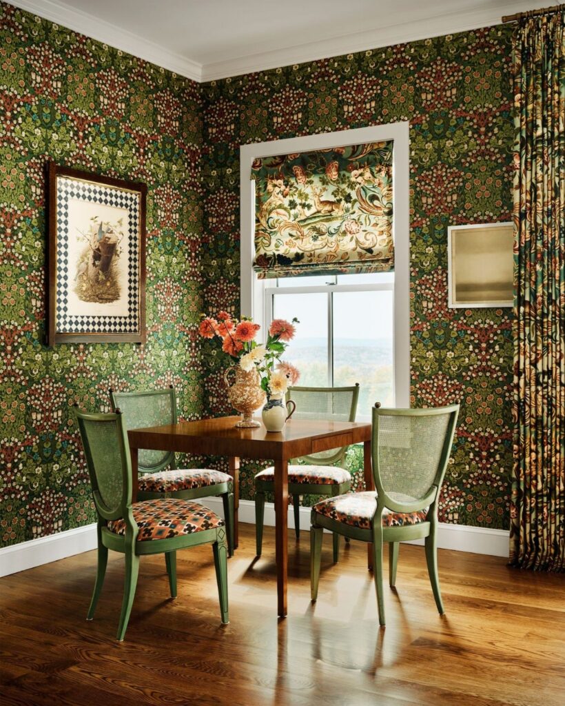 Small dining room with green floral wallpaper, wooden table, and four green cane-back chairs.