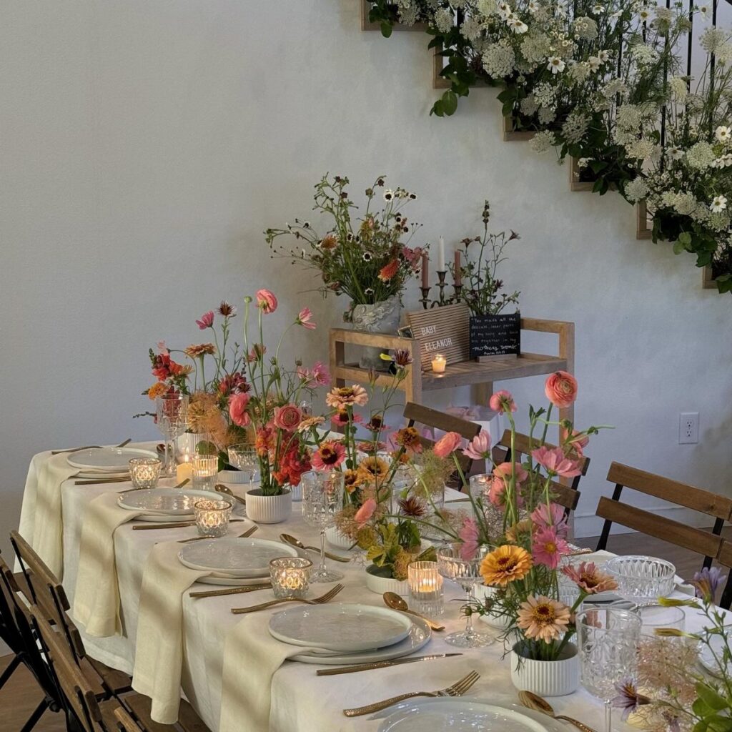 A long dining table decorated with colorful wildflowers, white plates, and glowing candles.