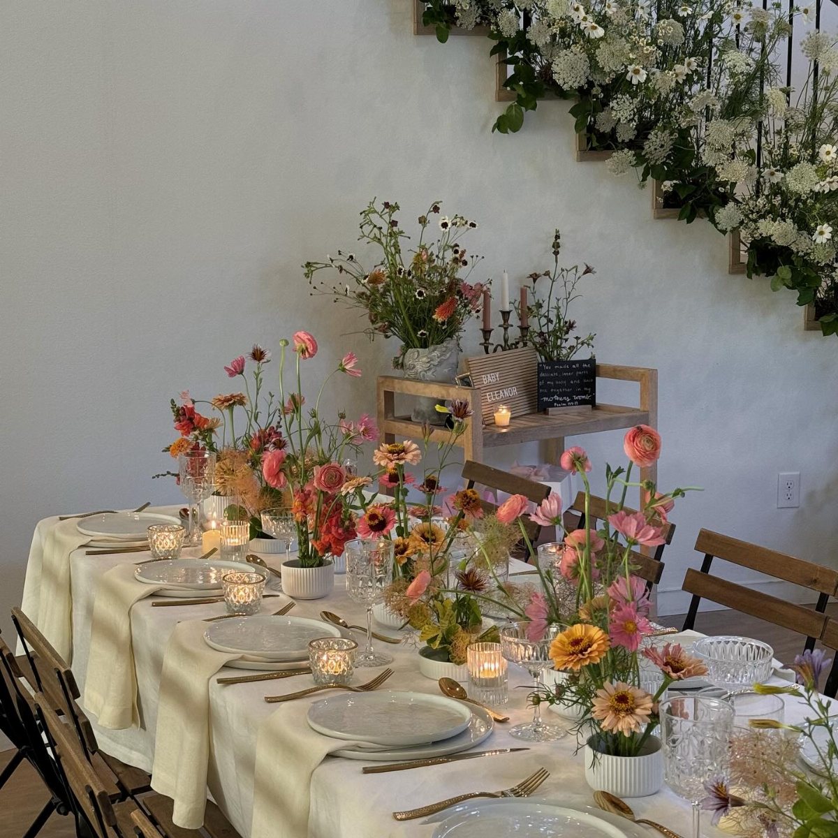 A long dining table decorated with colorful wildflowers, white plates, and glowing candles.