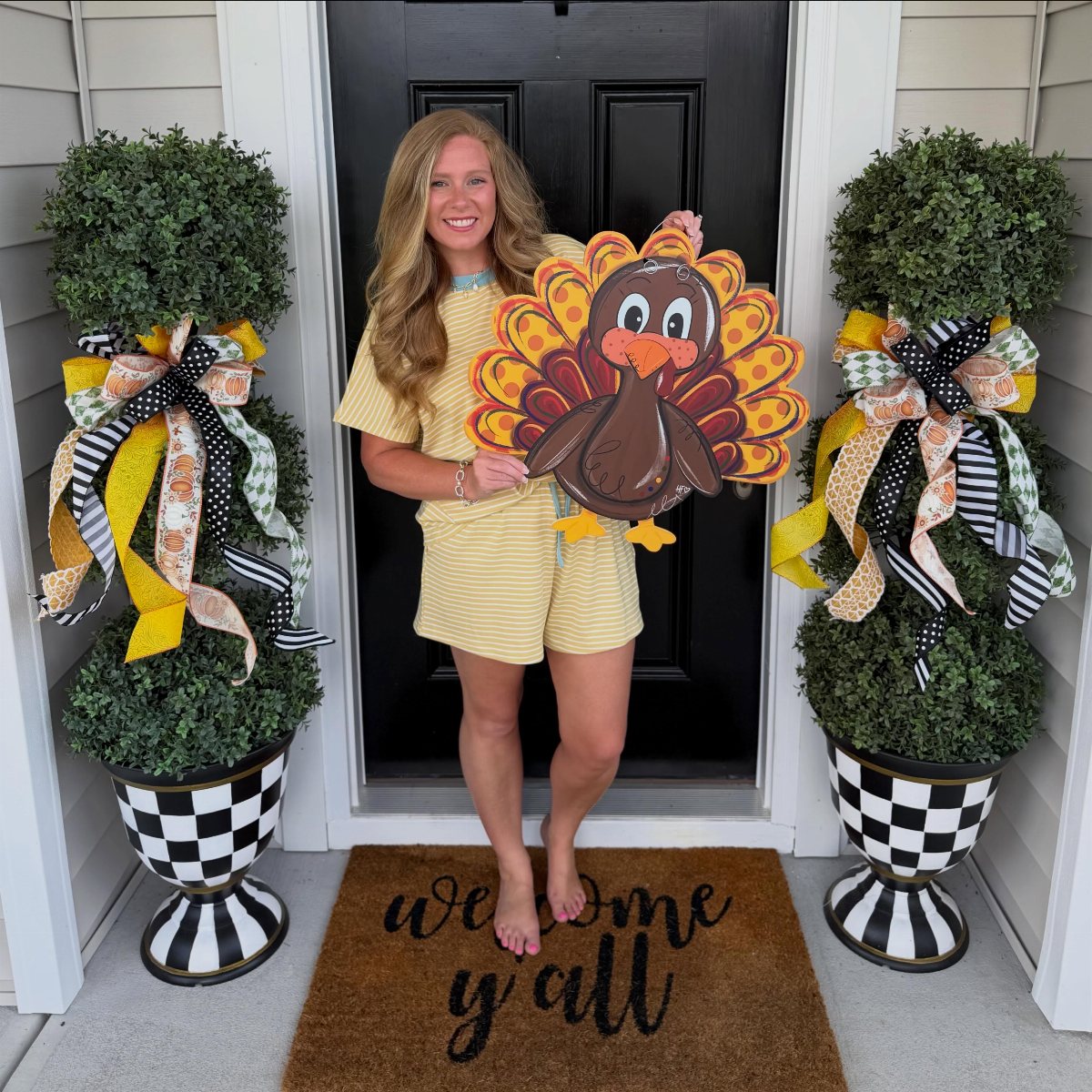 A woman holding a large decorative wooden turkey cutout in front of a black door.