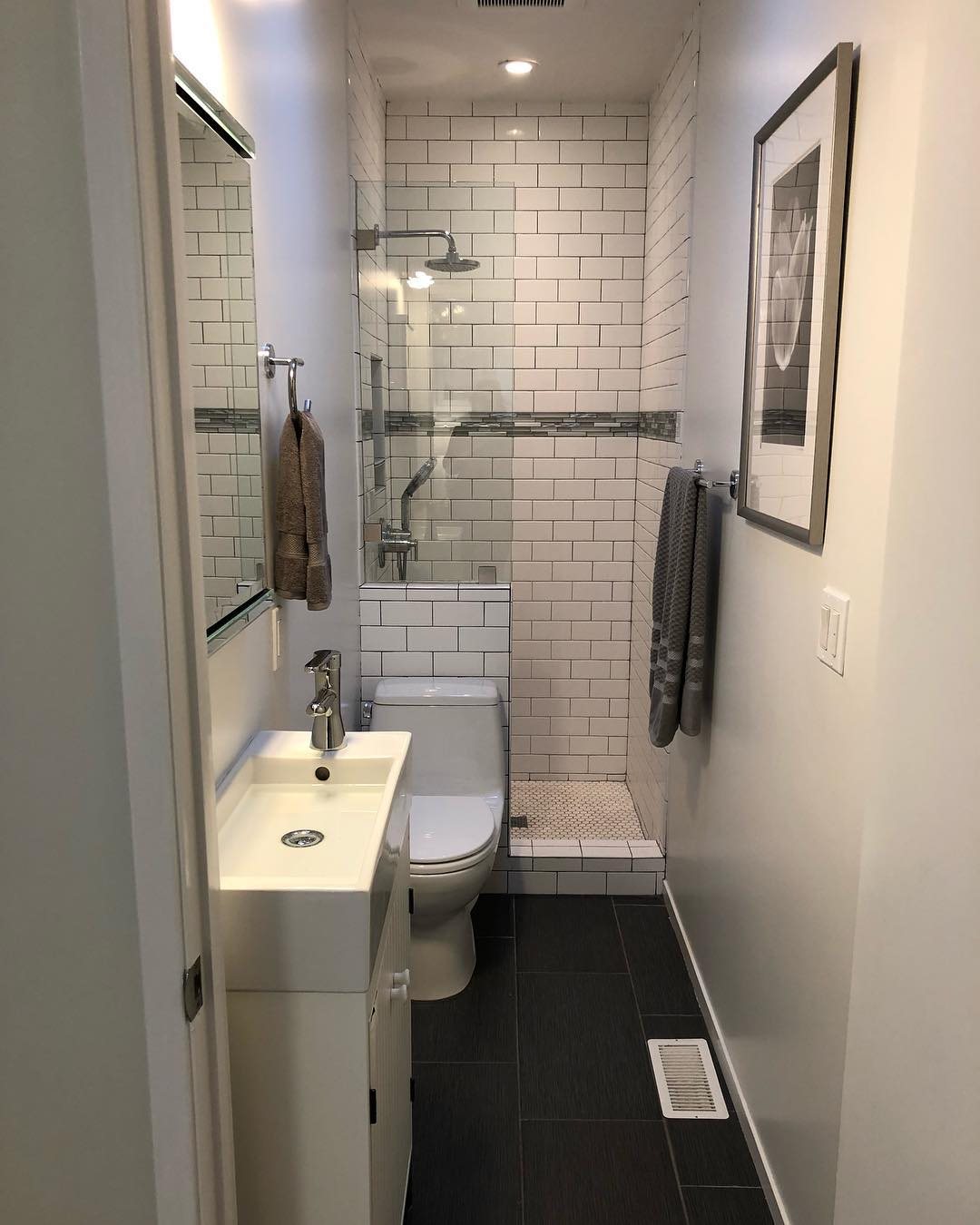 A narrow tiny bathroom with white subway tiles, a small sink, toilet, and glass shower.