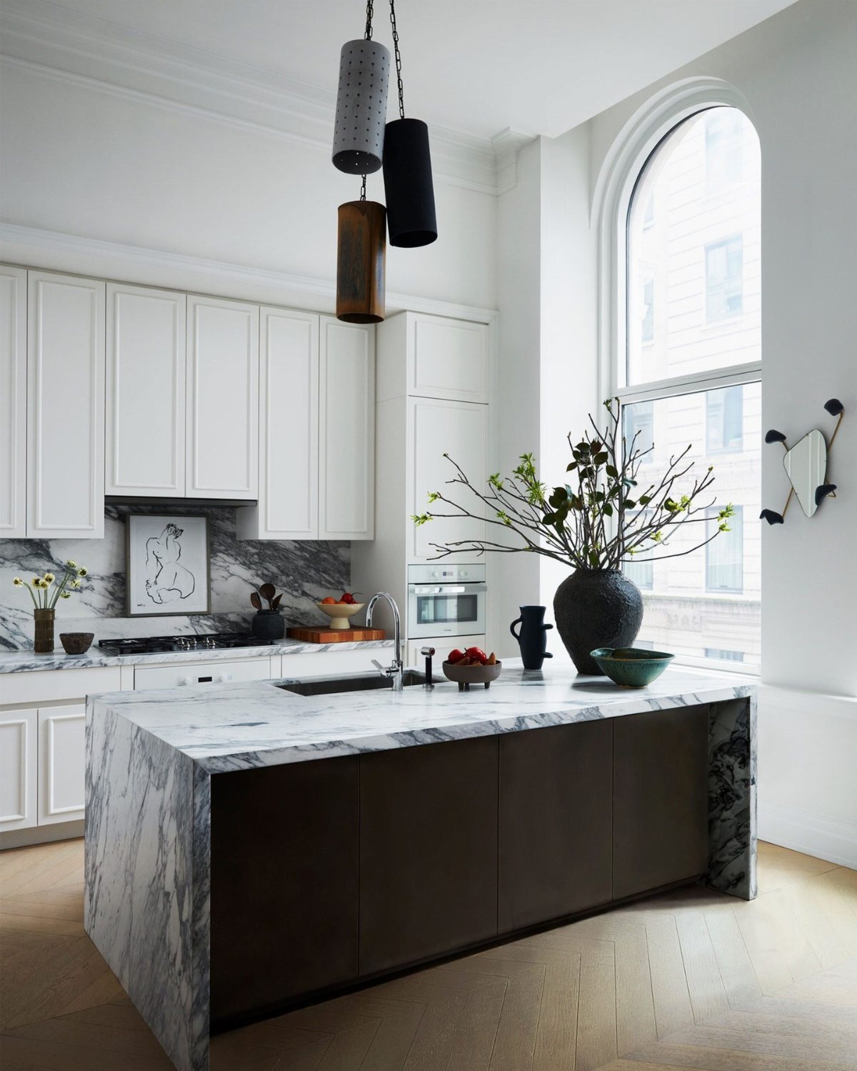 Modern white kitchen with marble island, white cabinetry, and large arched window.