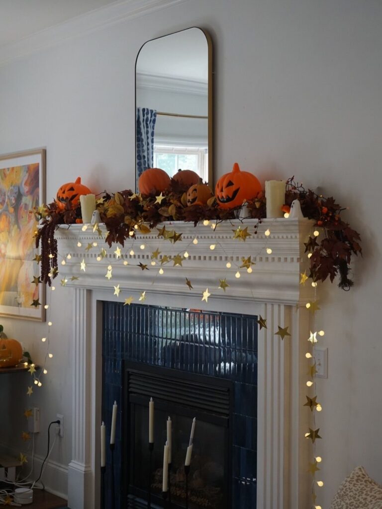 White fireplace mantel decorated with orange pumpkins, autumn leaves, and star-shaped fairy lights.