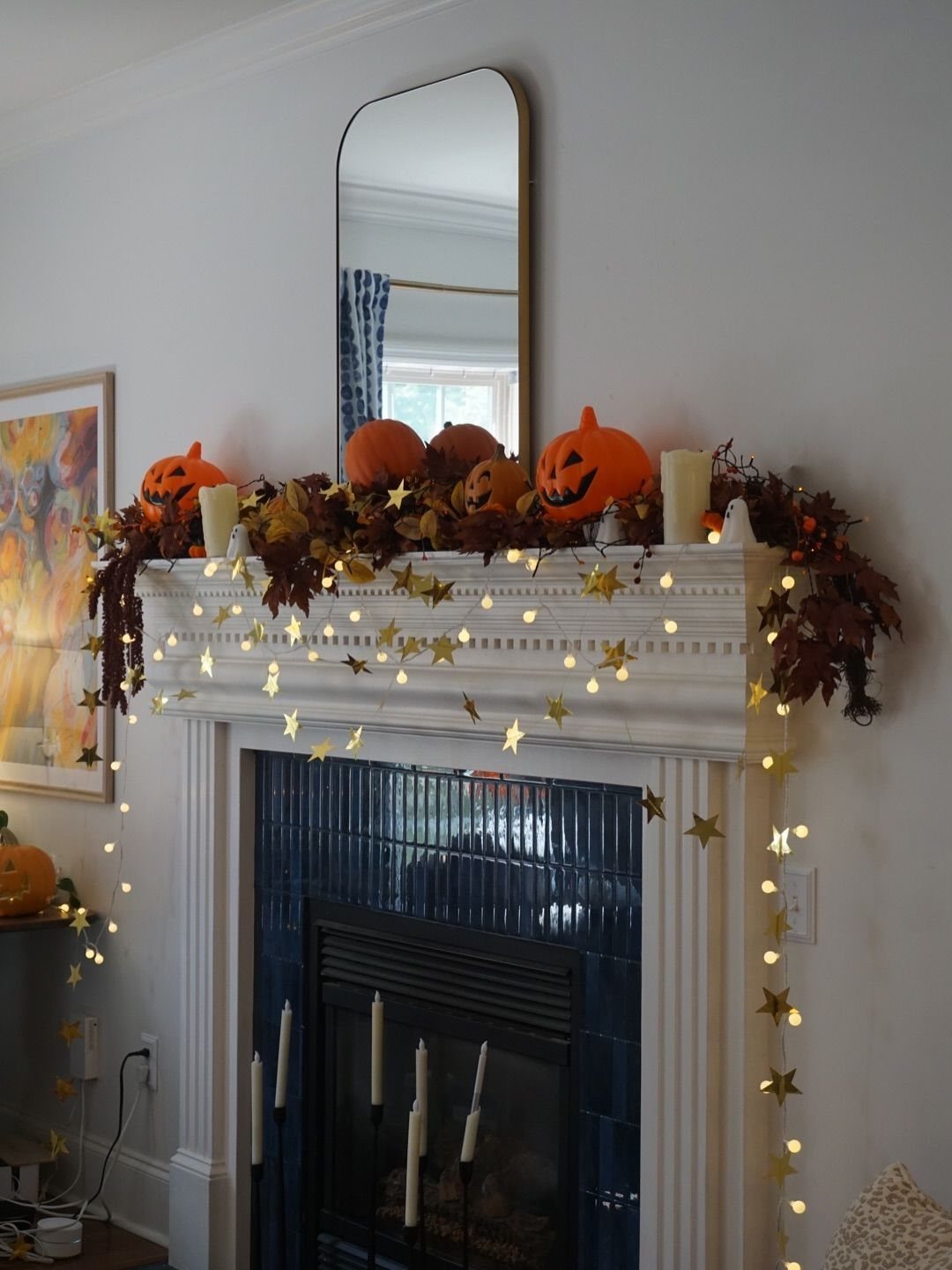 White fireplace mantel decorated with orange pumpkins, autumn leaves, and star-shaped fairy lights.