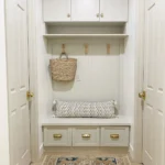 Built-in white mudroom nook with bench, storage drawers, wall hooks, and wicker baskets.