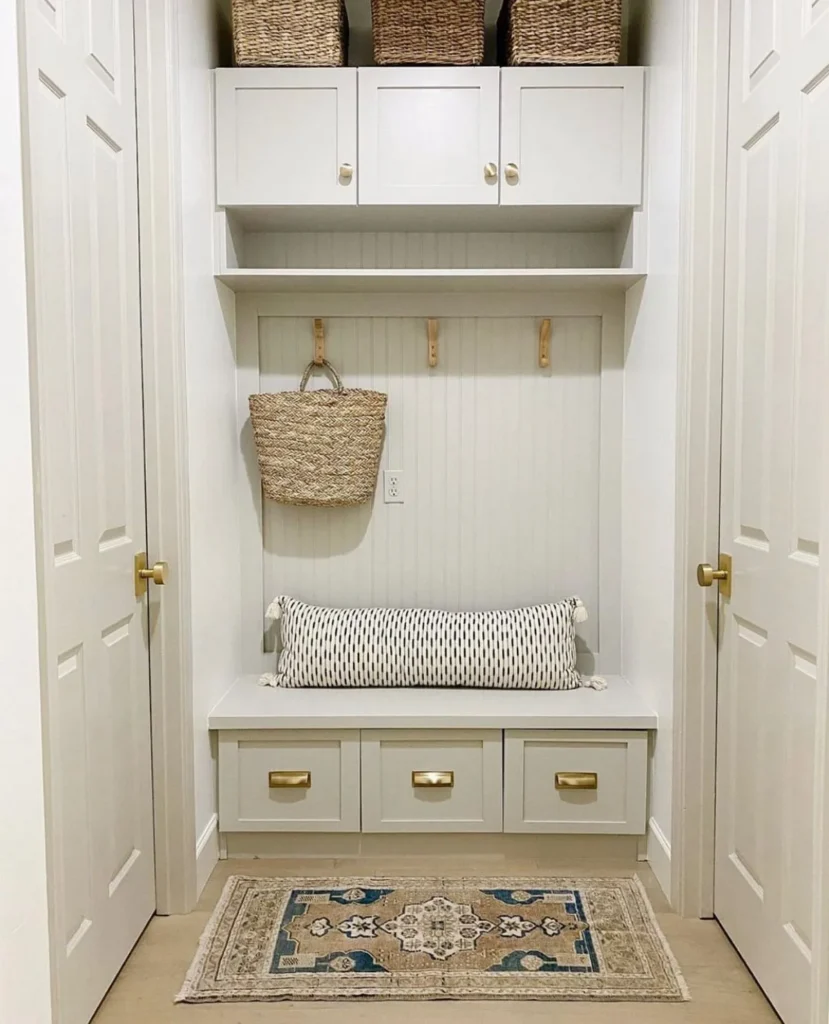 Built-in white mudroom nook with bench, storage drawers, wall hooks, and wicker baskets.